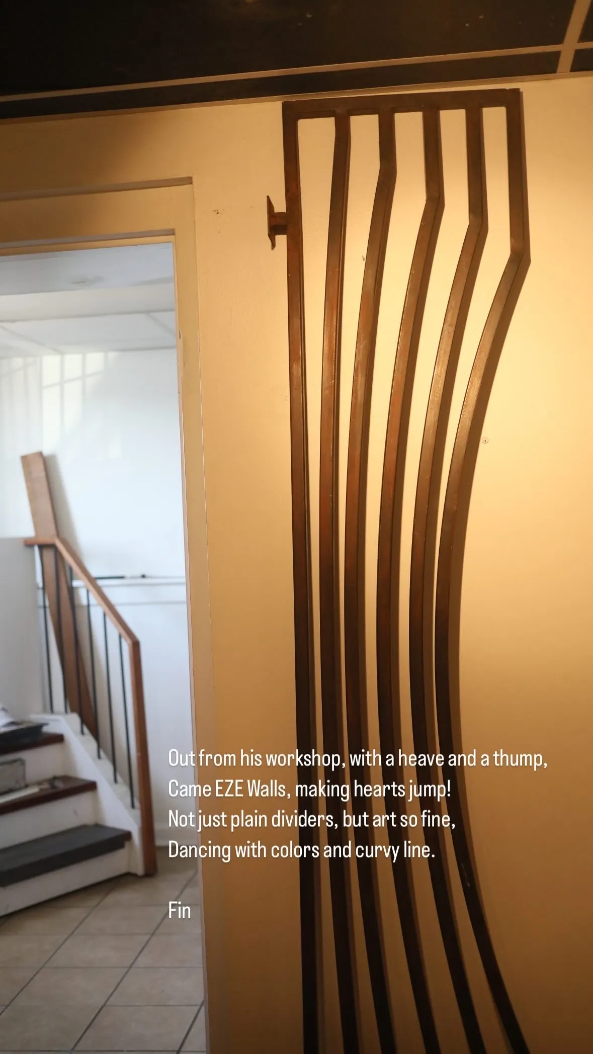 Curvy wooden wall divider mounted on a beige wall next to a staircase with tiled floor.